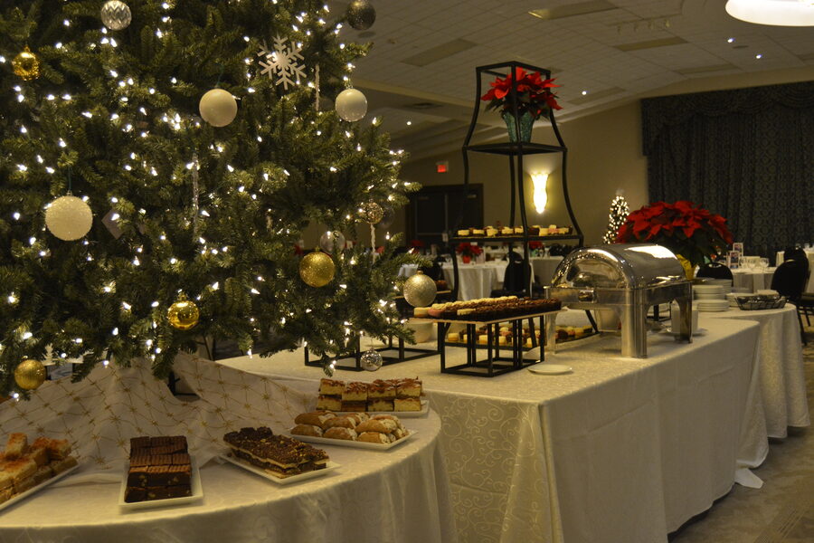 A holiday buffet table beside a decorated Christmas tree, set with desserts and a chafing dish