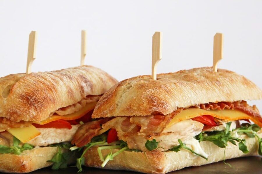 Grilled chicken, bacon and cheese ciabatta sandwiches on a dark wooden board