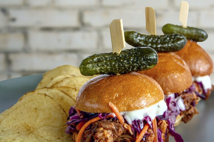 Pulled pork sliders on brioche buns with slaw and pickle picks beside kettle chips